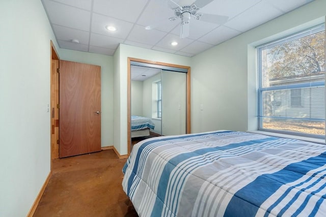 bedroom with a closet, a drop ceiling, ceiling fan, and baseboards