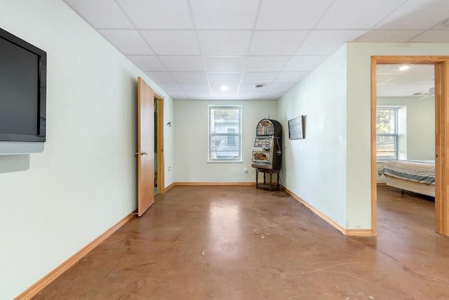 corridor featuring concrete flooring, a wealth of natural light, and a paneled ceiling