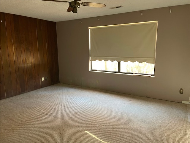 carpeted spare room with ceiling fan and wood walls