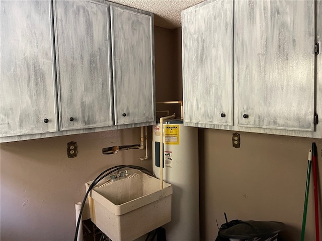 clothes washing area with sink, water heater, and a textured ceiling