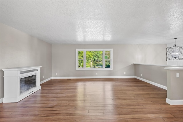 unfurnished living room featuring an inviting chandelier, dark hardwood / wood-style floors, and a textured ceiling