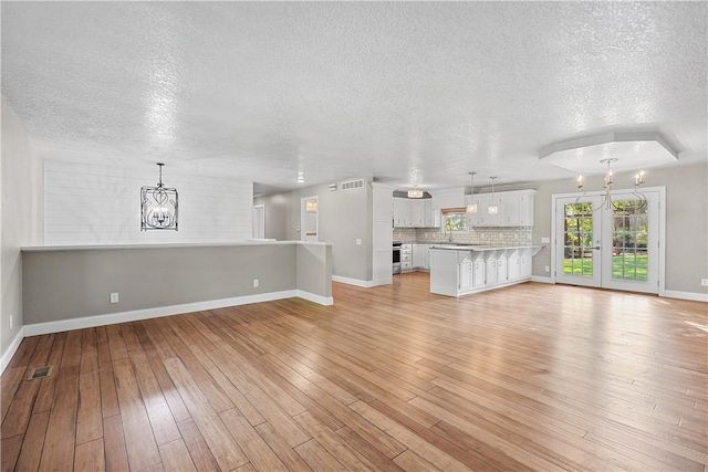 unfurnished living room featuring light wood-type flooring, sink, a textured ceiling, and an inviting chandelier