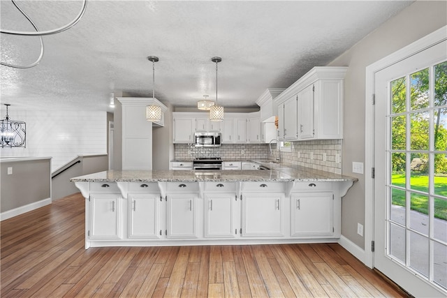 kitchen featuring pendant lighting, white cabinetry, stainless steel appliances, and light wood-type flooring