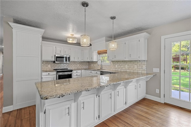 kitchen featuring light hardwood / wood-style flooring, kitchen peninsula, a healthy amount of sunlight, pendant lighting, and appliances with stainless steel finishes