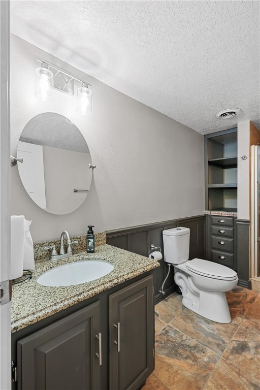 bathroom with toilet, wood walls, a textured ceiling, and vanity