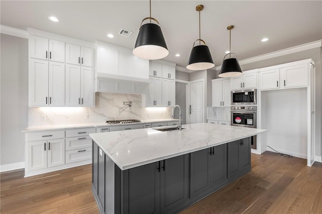 kitchen with a center island with sink, decorative light fixtures, white cabinetry, and light stone countertops