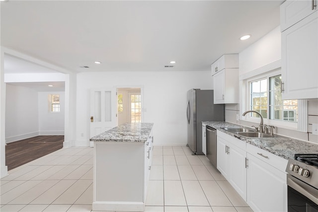 kitchen featuring light stone counters, stainless steel appliances, a kitchen island, and white cabinets