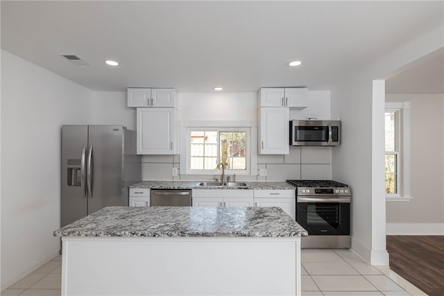 kitchen with appliances with stainless steel finishes, white cabinets, sink, and a kitchen island