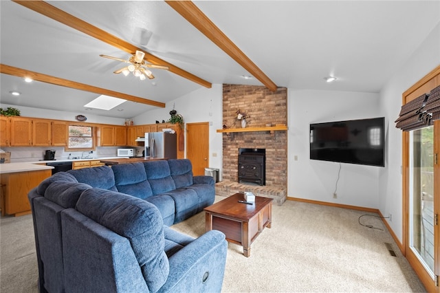 living area with light carpet, a ceiling fan, visible vents, baseboards, and lofted ceiling with skylight