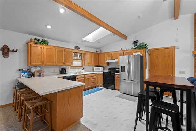 kitchen with a sink, a peninsula, vaulted ceiling with skylight, under cabinet range hood, and black appliances