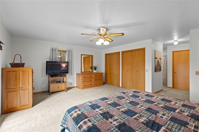 bedroom featuring light carpet, ceiling fan, baseboards, and multiple closets