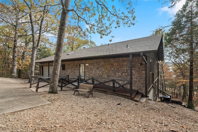 exterior space featuring stone siding and roof with shingles