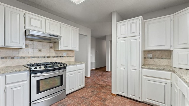 kitchen with stainless steel gas stove, backsplash, white cabinetry, and light stone countertops