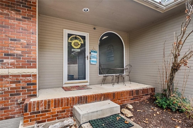 entrance to property with a porch and brick siding