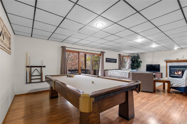 playroom featuring a glass covered fireplace, wood finished floors, a drop ceiling, billiards, and baseboards