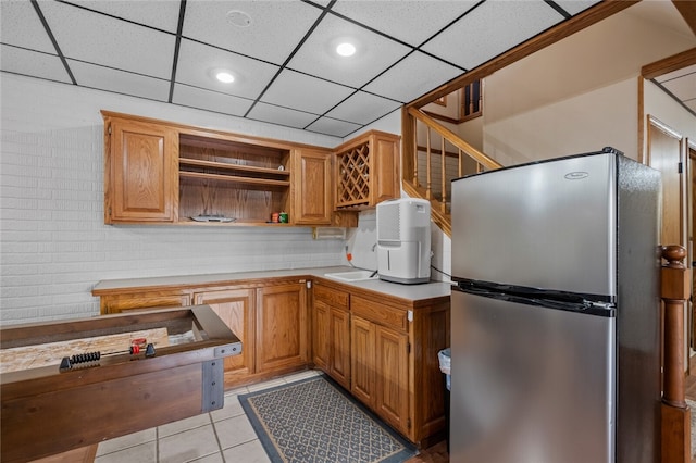 kitchen with light tile patterned floors, a drop ceiling, light countertops, freestanding refrigerator, and open shelves