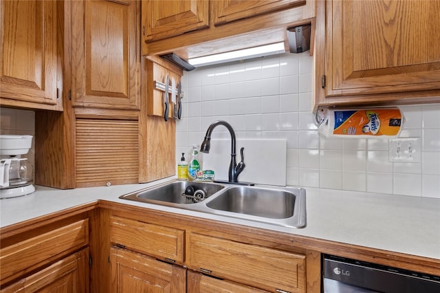 kitchen featuring light countertops, backsplash, brown cabinetry, a sink, and dishwashing machine