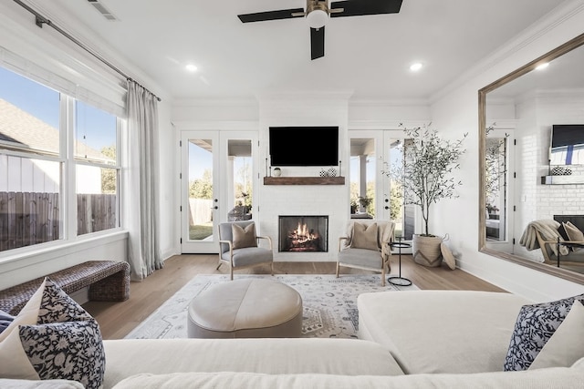 living room with french doors, ornamental molding, a fireplace, and light hardwood / wood-style flooring