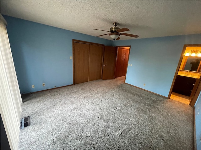 unfurnished bedroom featuring ensuite bathroom, a textured ceiling, a closet, ceiling fan, and light colored carpet