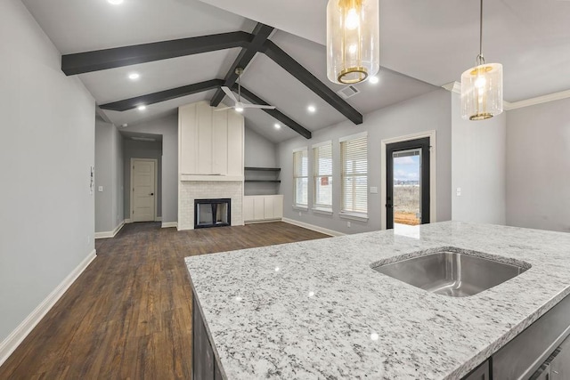 kitchen with pendant lighting, ceiling fan, vaulted ceiling with beams, a fireplace, and light stone countertops