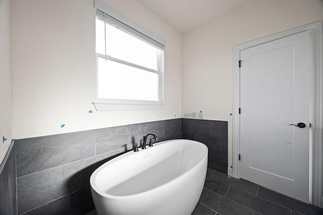 bathroom with tile patterned flooring, a soaking tub, tile walls, and a wainscoted wall