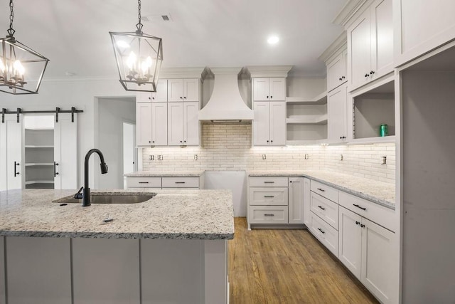 kitchen with premium range hood, sink, white cabinetry, decorative light fixtures, and a barn door