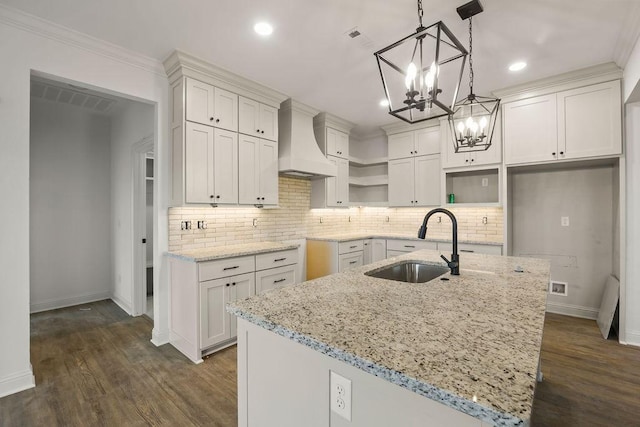 kitchen with pendant lighting, sink, an island with sink, and custom range hood