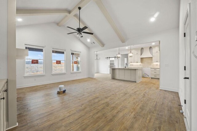 unfurnished living room featuring sink, light hardwood / wood-style flooring, ceiling fan, high vaulted ceiling, and beamed ceiling