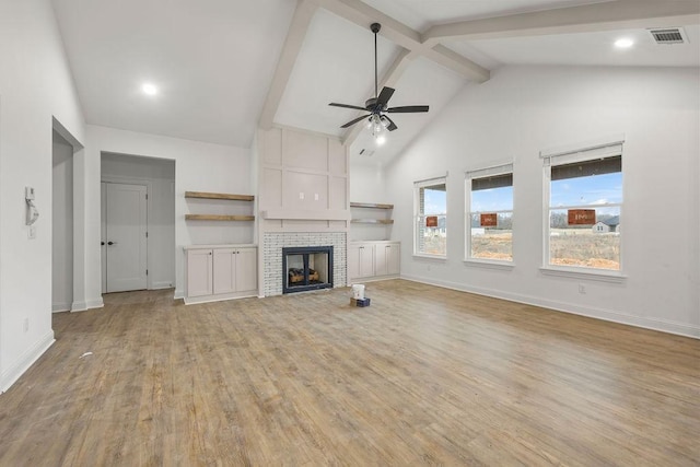 unfurnished living room featuring ceiling fan, beam ceiling, high vaulted ceiling, a fireplace, and light hardwood / wood-style floors