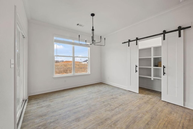 unfurnished dining area with crown molding, light hardwood / wood-style floors, a barn door, and a chandelier