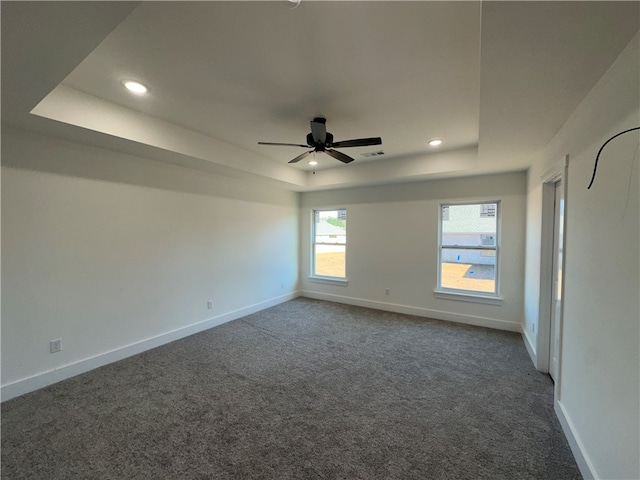 unfurnished room with dark colored carpet, ceiling fan, and a raised ceiling