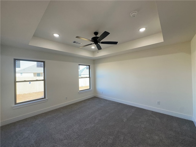 unfurnished room featuring a tray ceiling, ceiling fan, and dark colored carpet