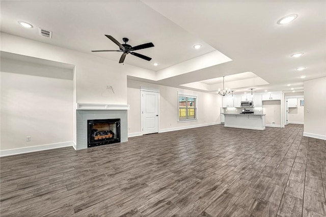 unfurnished living room featuring baseboards, visible vents, dark wood finished floors, a raised ceiling, and ceiling fan with notable chandelier