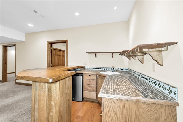 kitchen with light brown cabinetry, sink, kitchen peninsula, and light hardwood / wood-style floors