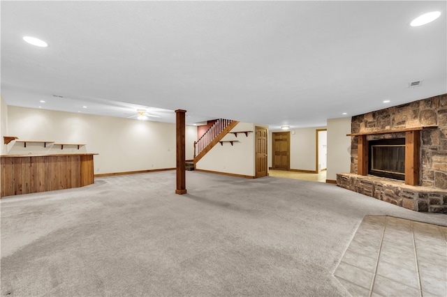 basement featuring ceiling fan, a stone fireplace, and light colored carpet