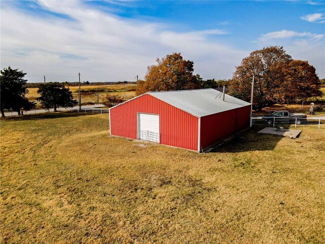 view of outdoor structure featuring a rural view, a garage, and a lawn