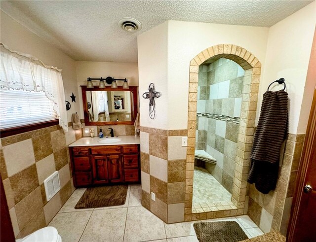 bathroom featuring tile patterned floors, vanity, tile walls, a textured ceiling, and walk in shower