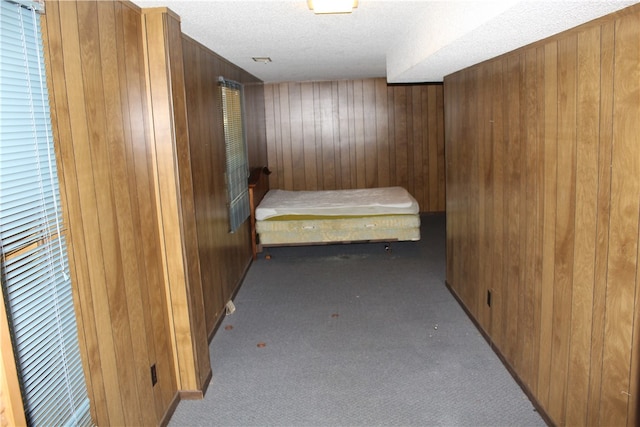 hallway featuring light carpet, wood walls, and a textured ceiling