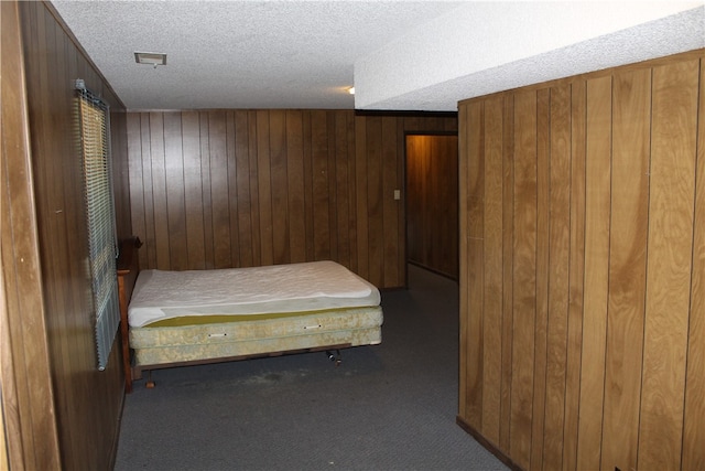 unfurnished bedroom with carpet flooring, a textured ceiling, and wood walls