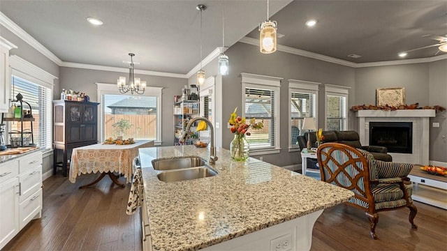 kitchen with light stone counters, decorative light fixtures, white cabinets, a sink, and an island with sink