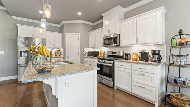 kitchen with pendant lighting, appliances with stainless steel finishes, a center island with sink, and white cabinets