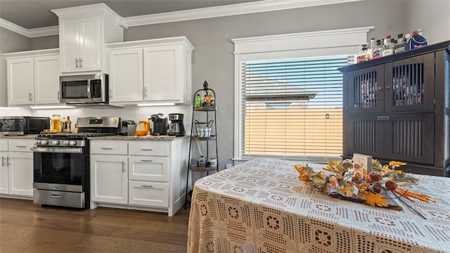 kitchen featuring stone countertops, white cabinets, ornamental molding, appliances with stainless steel finishes, and dark wood finished floors