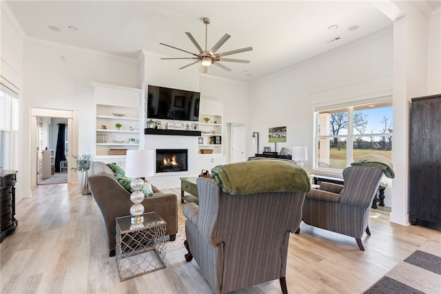 living room featuring a towering ceiling, crown molding, a large fireplace, and light wood-type flooring