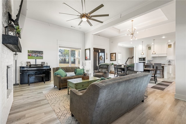 living room with light hardwood / wood-style floors, crown molding, a fireplace, and ceiling fan with notable chandelier