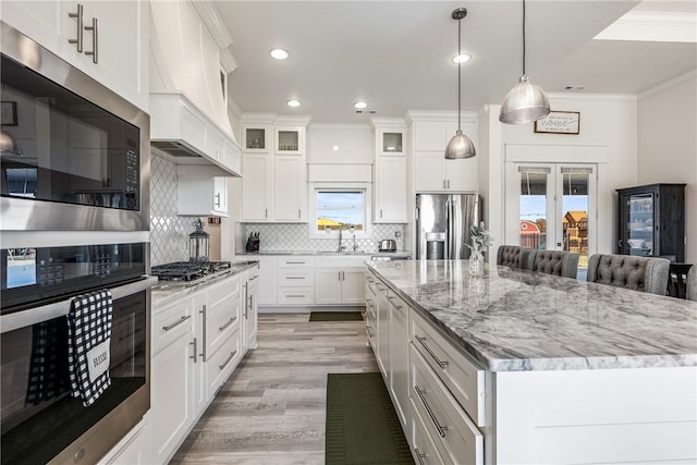 kitchen with appliances with stainless steel finishes, a center island, pendant lighting, white cabinets, and ornamental molding