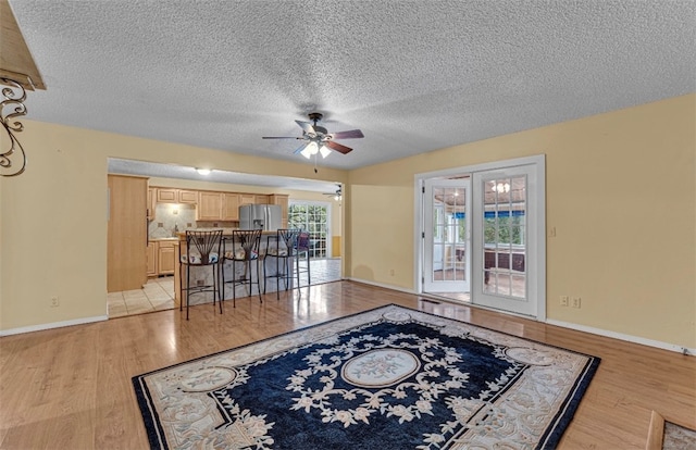 living room with a textured ceiling, light wood-type flooring, and ceiling fan