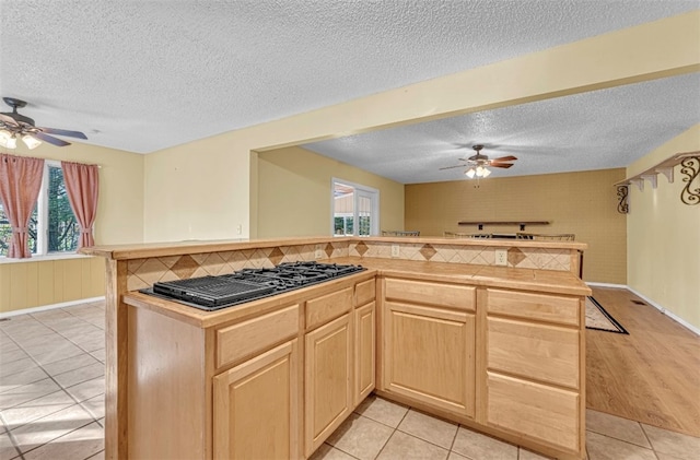 kitchen with light wood-type flooring, light brown cabinetry, stainless steel gas stovetop, a textured ceiling, and ceiling fan