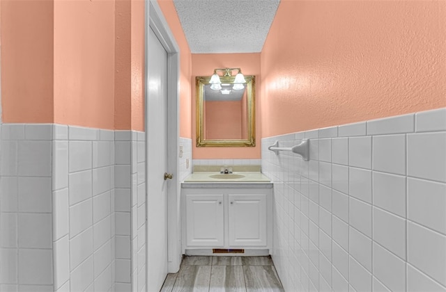 bathroom with vanity, a textured ceiling, wood-type flooring, and tile walls