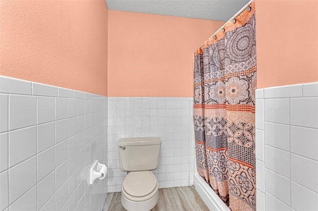 bathroom with toilet, wood-type flooring, curtained shower, tile walls, and a textured ceiling