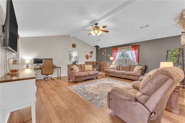 living room featuring ceiling fan, a wood stove, vaulted ceiling with beams, and light hardwood / wood-style flooring